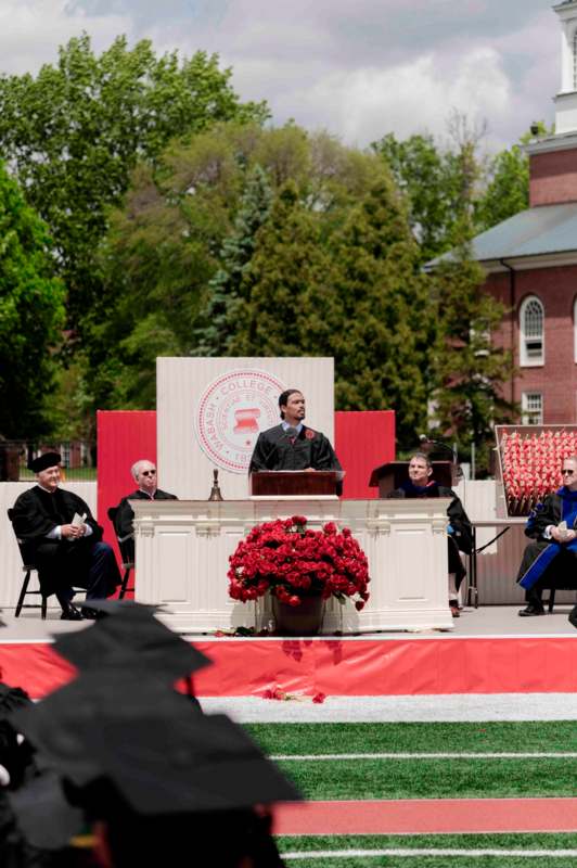 a man standing at a podium with a group of people sitting in chairs