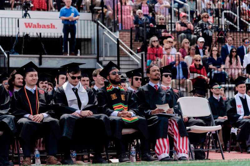 a group of people in graduation gowns and caps sitting in chairs