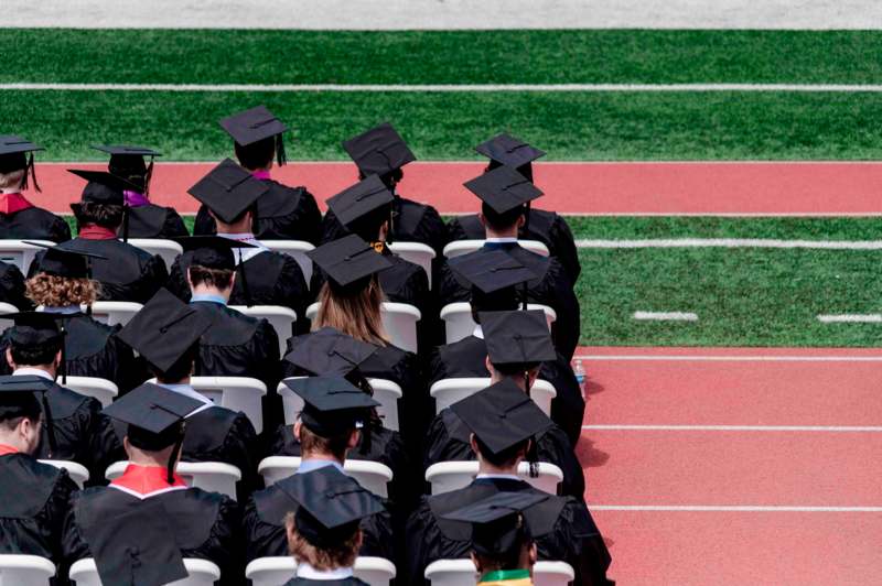 a group of people in graduation gowns and caps sitting in chairs on a track