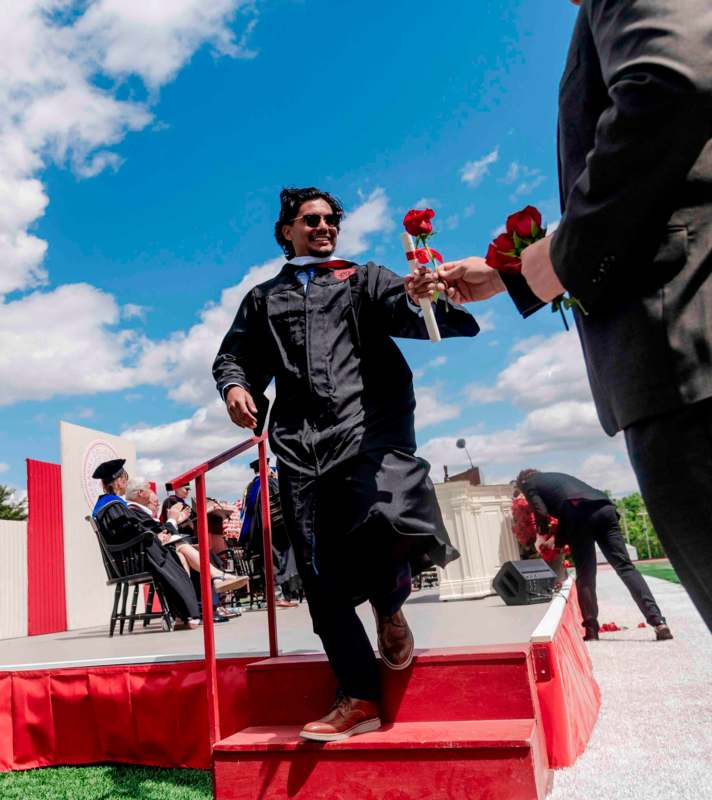 a man in a graduation gown holding a bouquet of roses