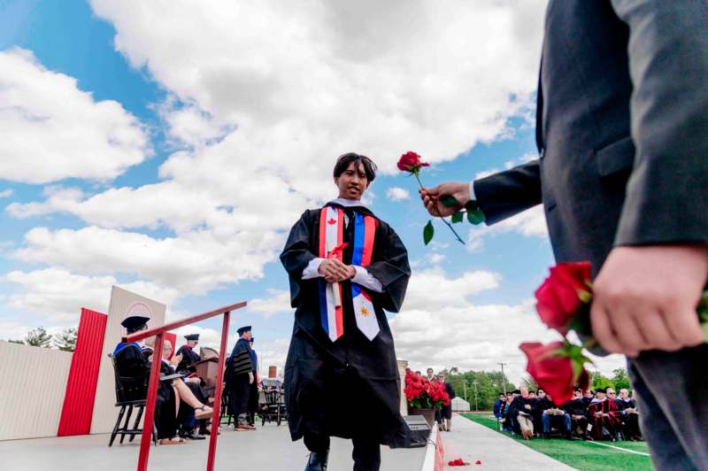 a man in a graduation gown giving a rose to a man