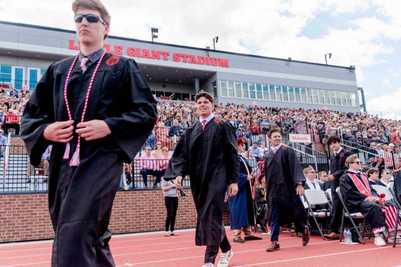 a group of men in graduation gowns walking on a track