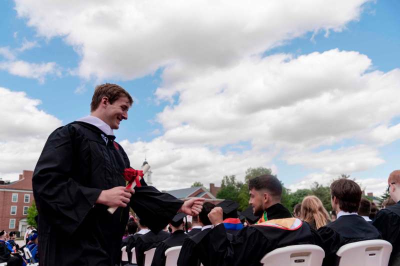 a man in a graduation gown giving a rose to another man