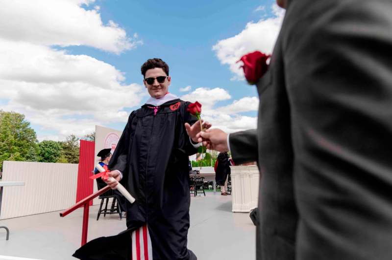 a man in a graduation gown holding a rose and a man in a black robe
