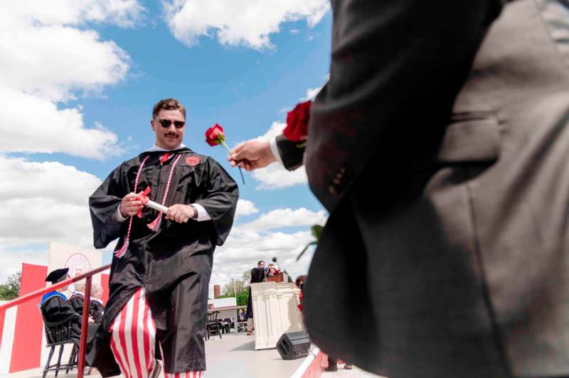 a man in a graduation gown holding a rose