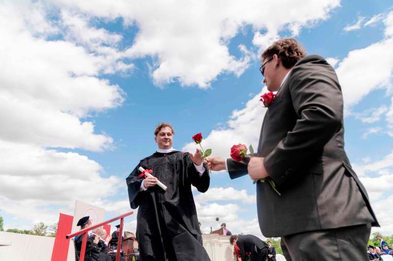 a man in a black robe giving a man a rose to another man