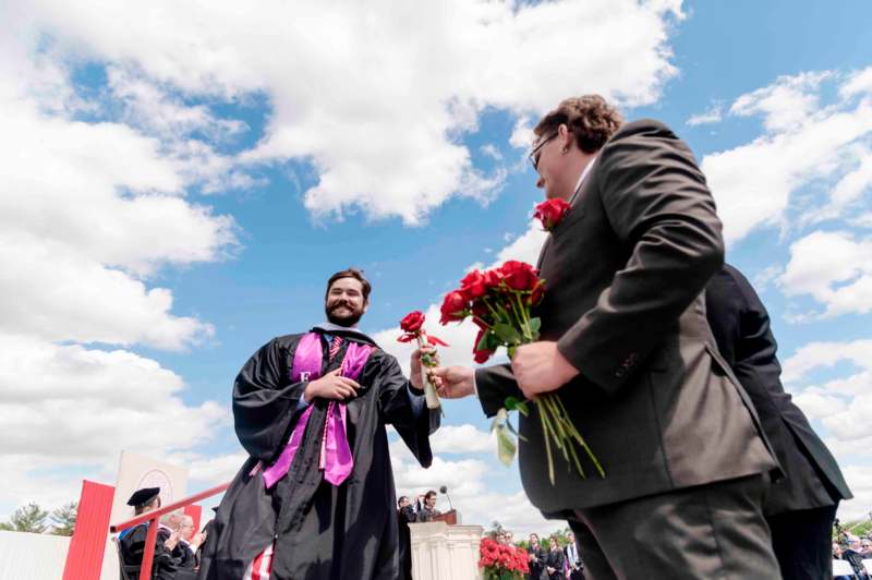 a man in a robe giving a man a bouquet of flowers to another man
