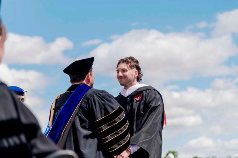 a man in a graduation gown shaking hands with another man