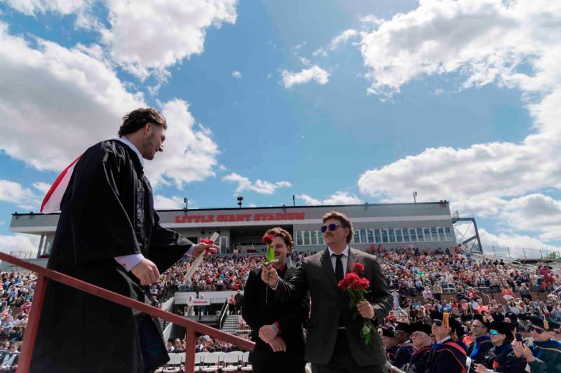 a man in a robe holding flowers and a man in a suit standing in front of a crowd