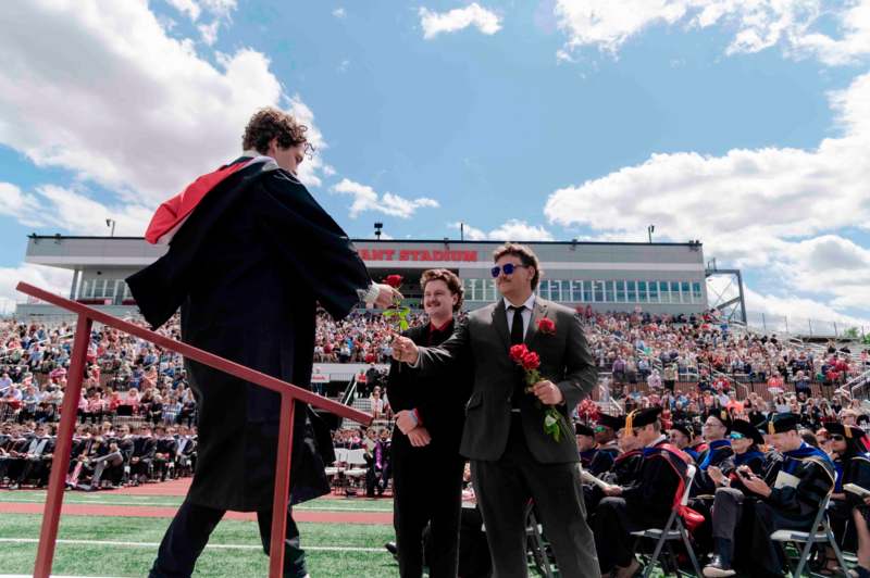 a man in a robe and a red cape receiving a flower from another man