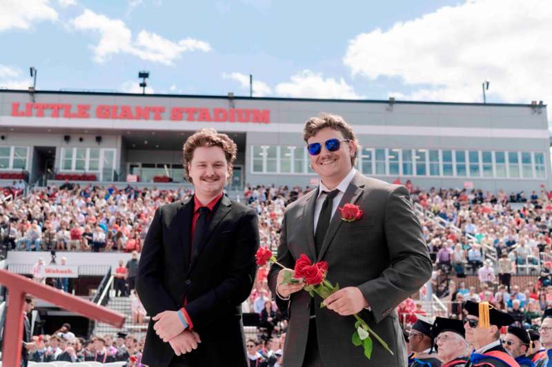 two men in suits holding flowers and standing in front of a stadium