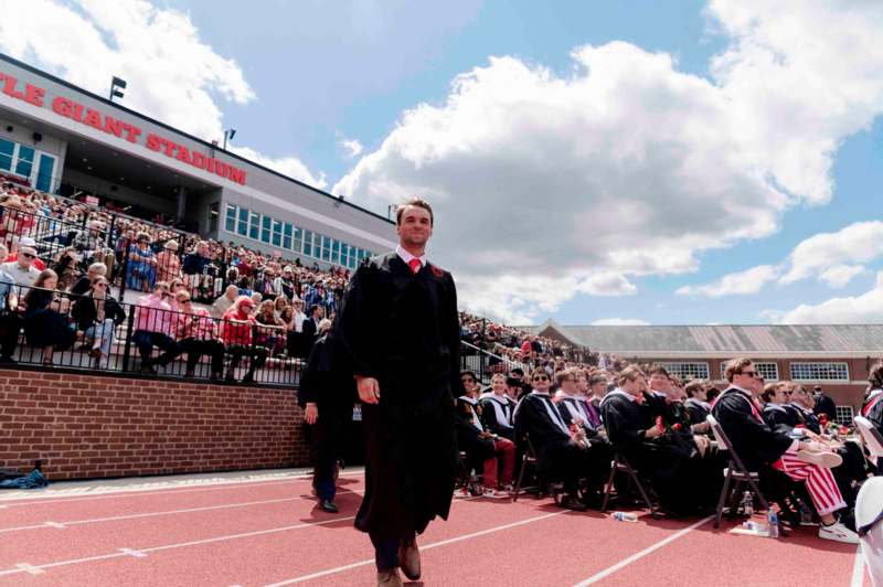 a man in a graduation gown walking on a track with a crowd of people