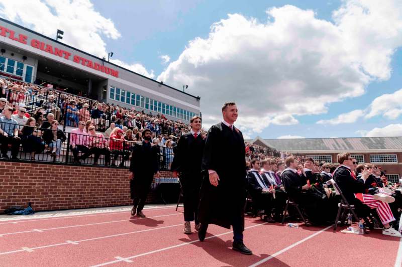 a group of men in graduation gowns walking on a track