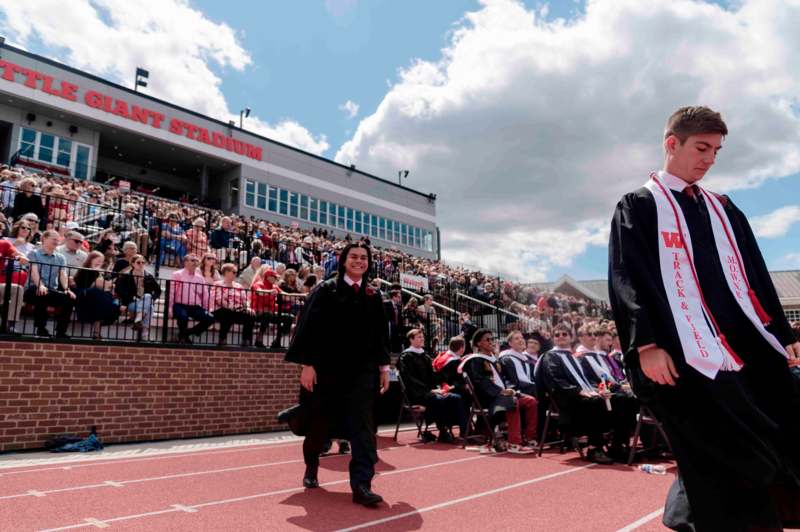 a man in a graduation gown walking on a track with a crowd watching