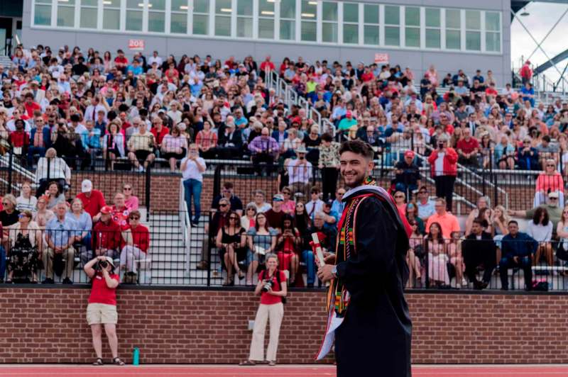 a man in a graduation gown holding a diploma in front of a crowd