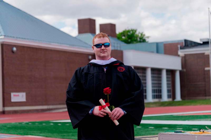 a man in a graduation gown holding a rose and diploma