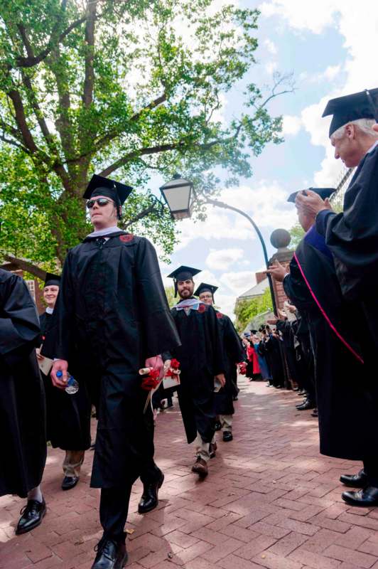 a group of people in graduation gowns and caps walking down a sidewalk