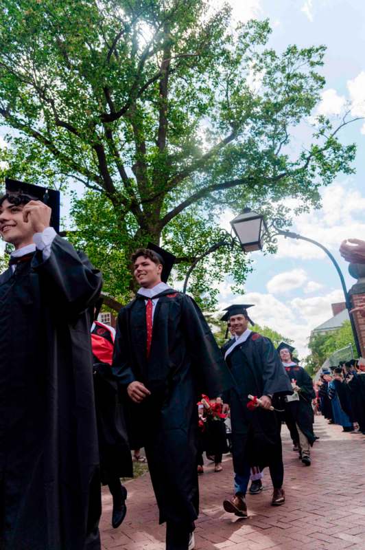 a group of people in graduation gowns and caps walking down a sidewalk