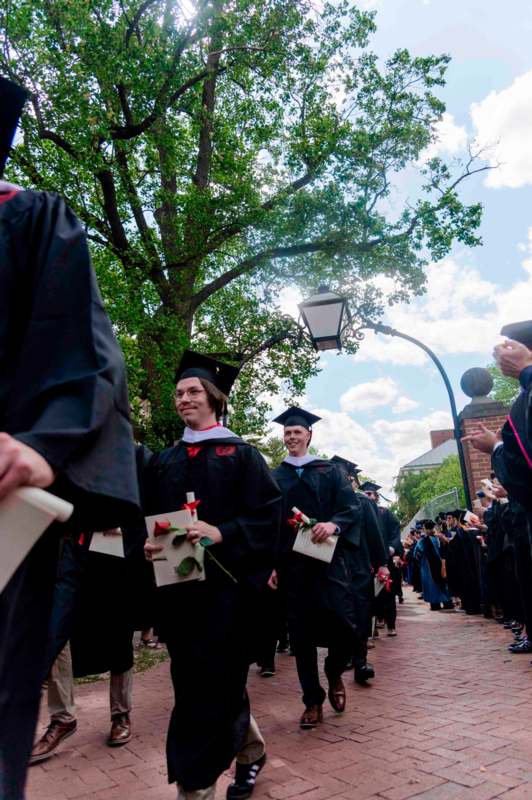 a group of people in graduation gowns and caps walking down a sidewalk
