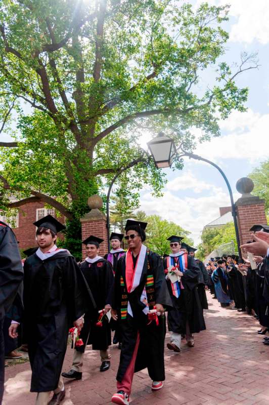 a group of people in graduation gowns and caps walking down a sidewalk