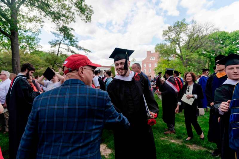 a man in a cap and gown shaking hands with a man in a red cap