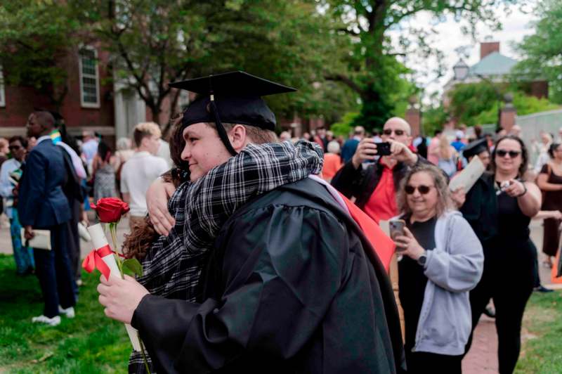 a man in a graduation gown hugging a woman with a rose