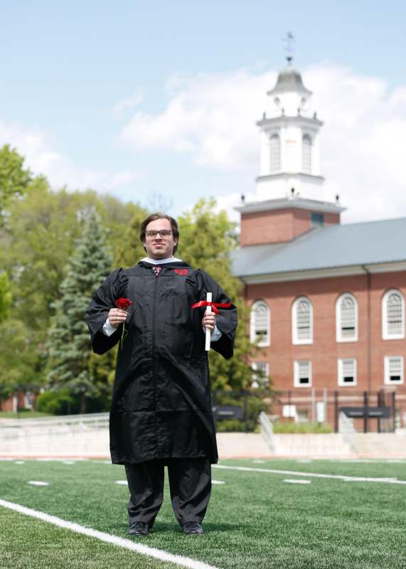 a man in a graduation gown holding a diploma and a red rose