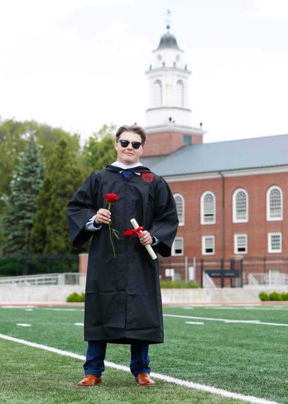 a man in a graduation gown holding a rose and a diploma
