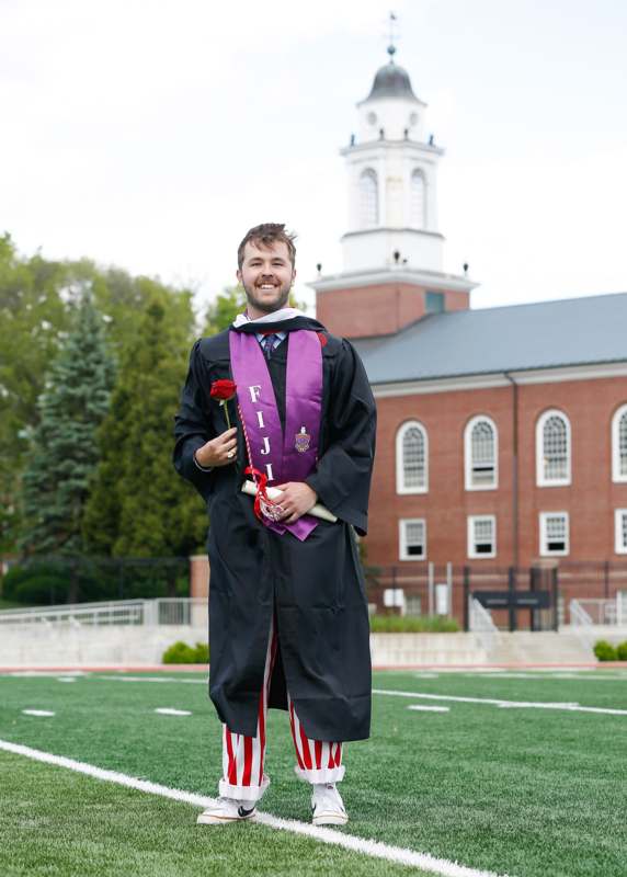 a man in a graduation gown holding a rose and a red rose