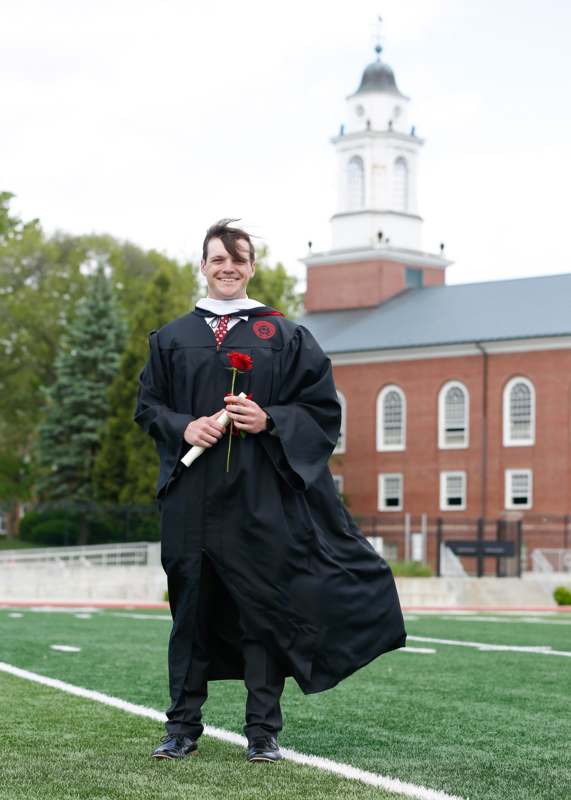 a man in a graduation gown holding a rose