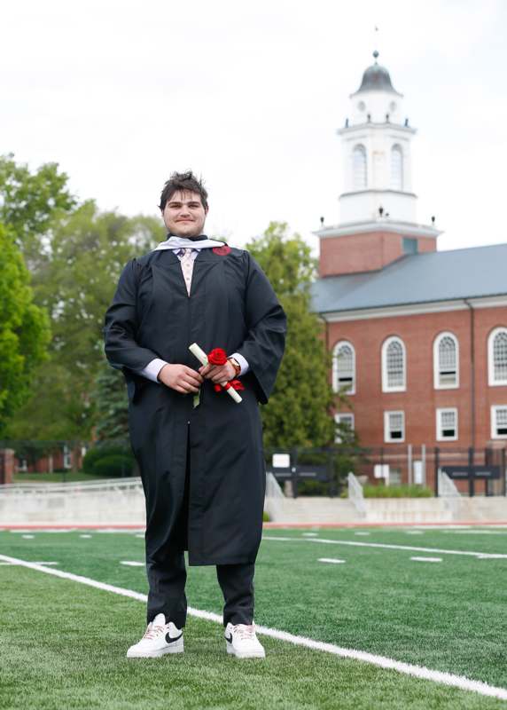 a man in a graduation gown holding a rose and a diploma