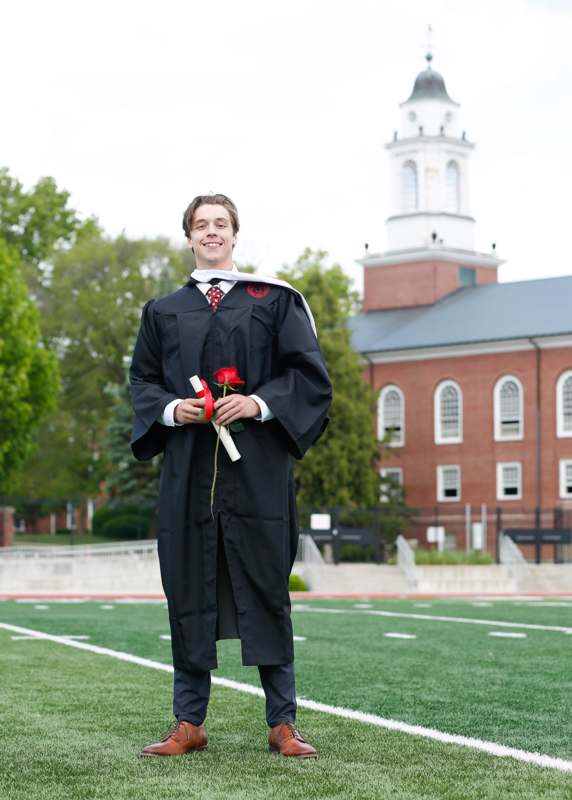a man in a graduation gown holding a rose and a diploma
