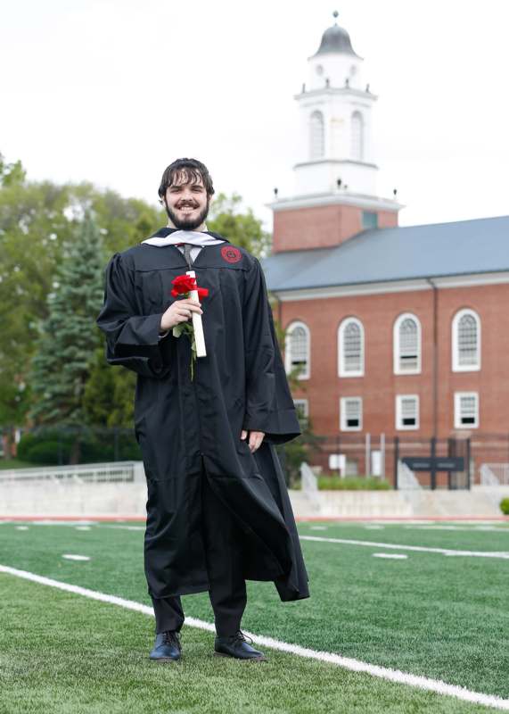 a man in a graduation gown holding a rose