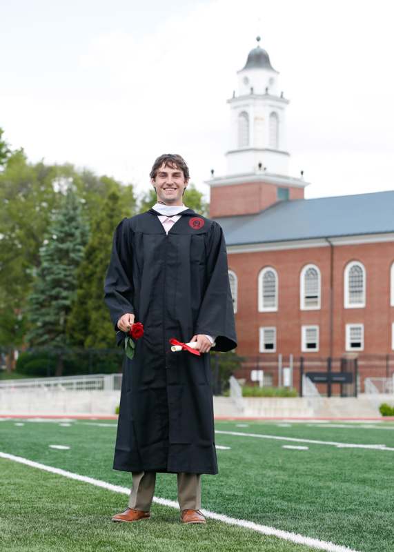 a man in a graduation gown holding a rose and standing on a football field