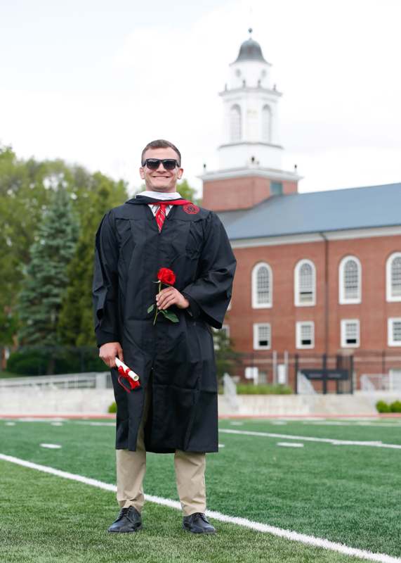 a man in a graduation gown holding a rose and a diploma