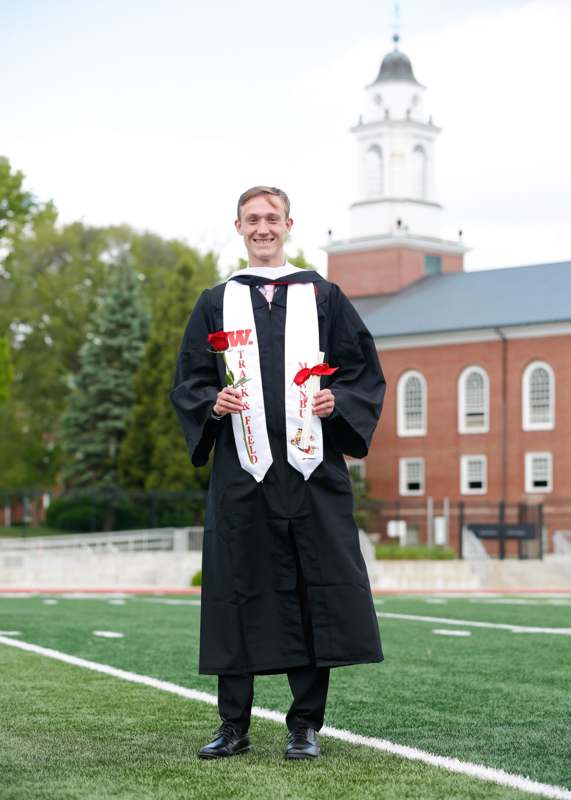 a man in a graduation gown holding a white sash and flowers