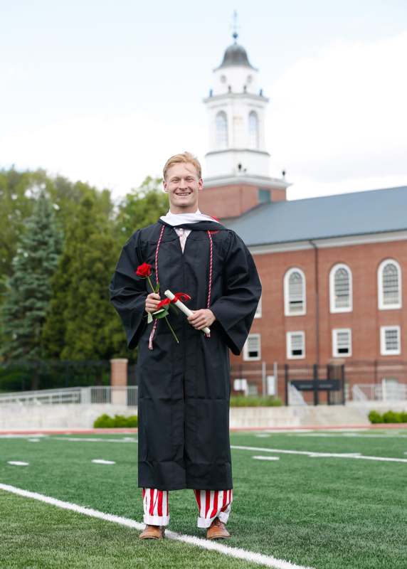 a man in a graduation gown holding a rose and diploma