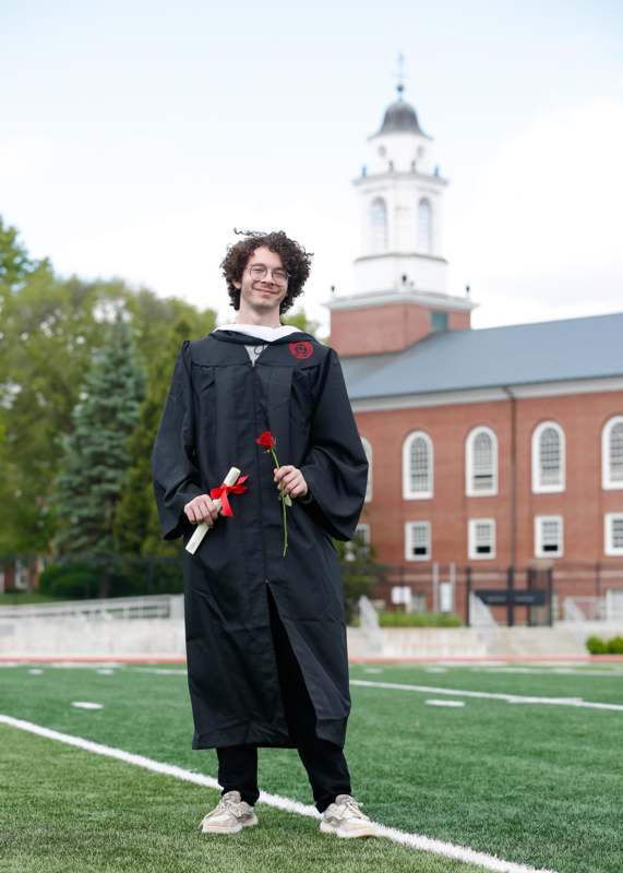 a man in a graduation gown holding a rose and a diploma