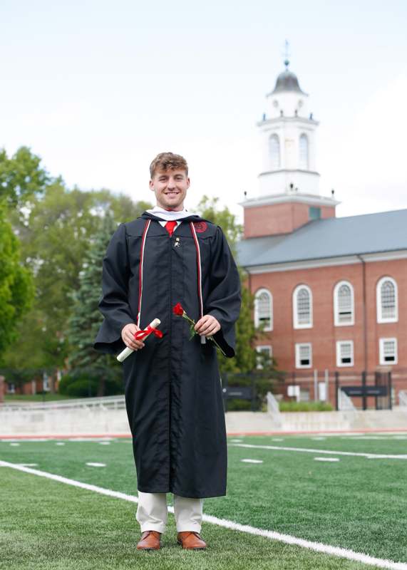 a man in a graduation gown holding a rose and diploma