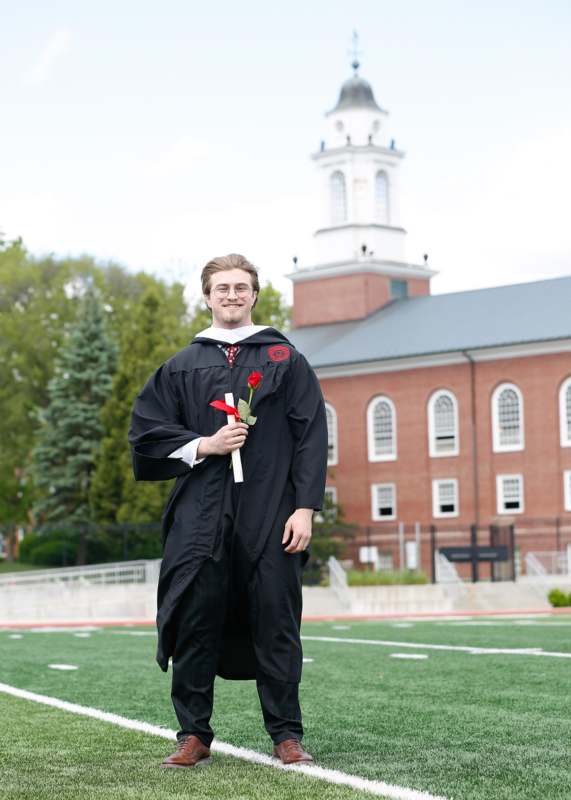 a man in a graduation gown holding a rose