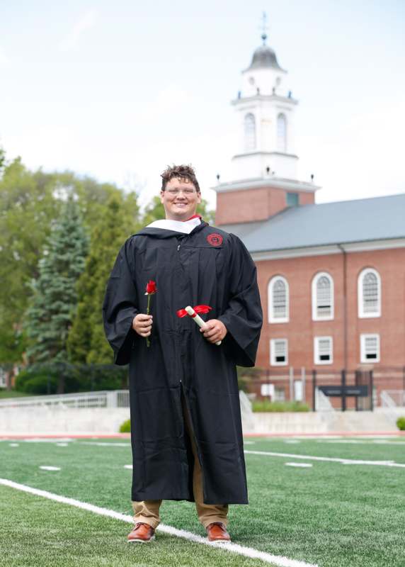 a man in a graduation gown holding a rose and diploma
