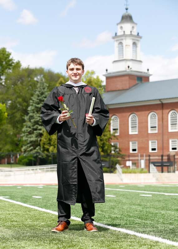 a man in a graduation gown holding a rose and diploma