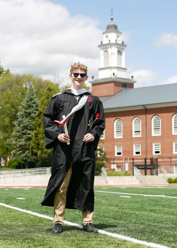 a man in a graduation gown holding a rose and a diploma