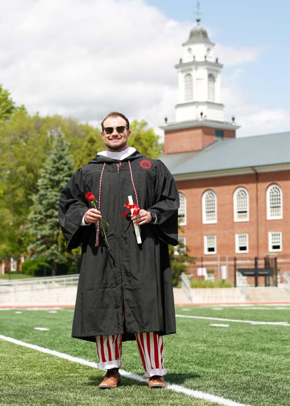 a man wearing a graduation gown and holding flowers