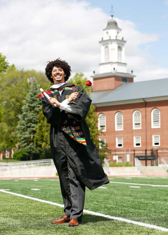 a man in a graduation gown holding a rose and a diploma