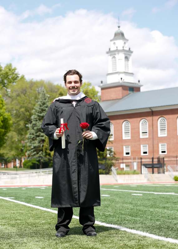 a man in a graduation gown holding a rose and a diploma