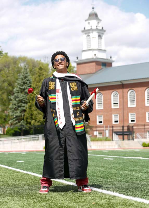 a man in a graduation gown holding a rose and a diploma