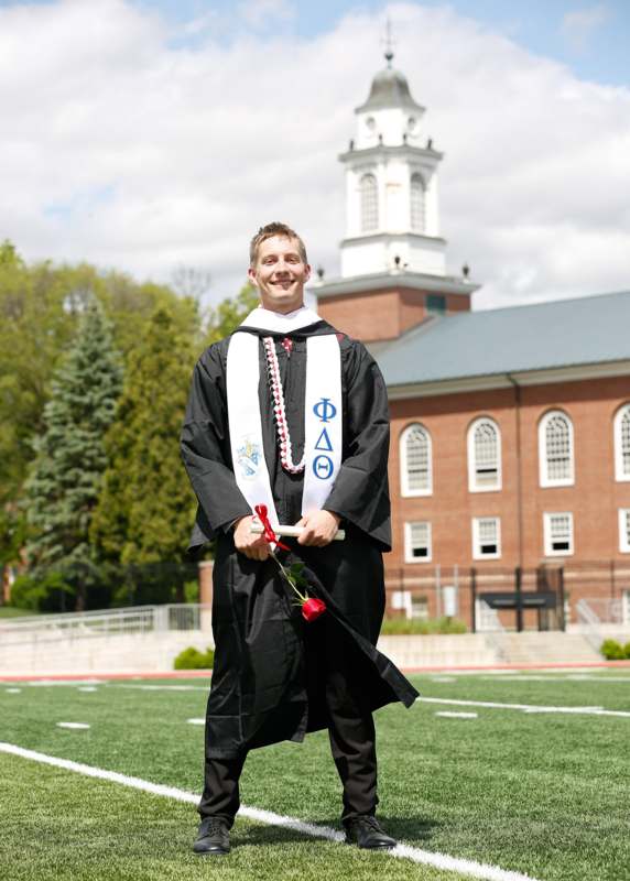 a man in a graduation gown holding a rose and a diploma
