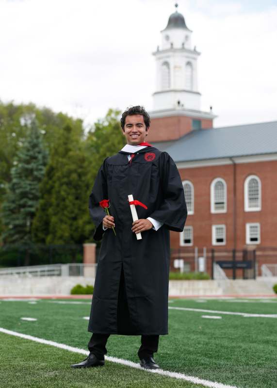 a man in a graduation gown holding a diploma and a rose
