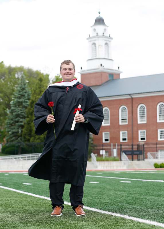 a man in a graduation gown holding a rose and a diploma